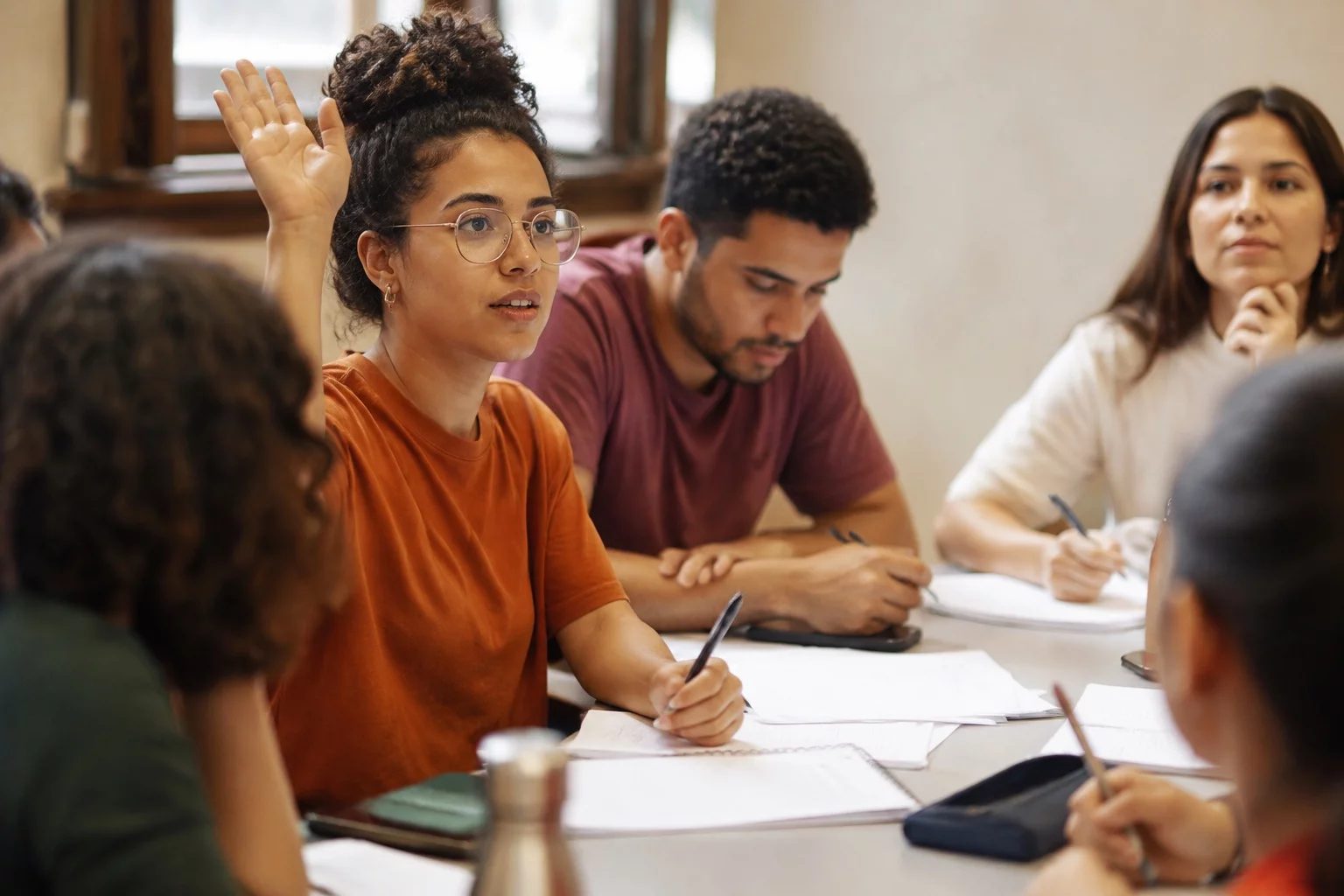 Estudante levantando a mão em uma mesa de seminário coberta de anotações